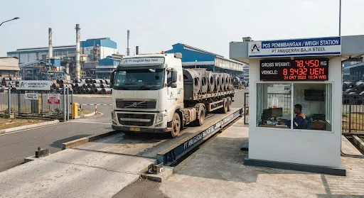 Massive truck weighbridge facility at the factory gate with an 80-ton digital weighing scale platform, a large logistics truck parked on the scale with the digital weight indicator display showing in clear numbers and the operator booth alongside.
